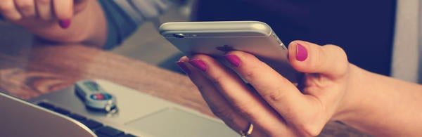 hand holding cellphone above computer (c) William Iven unsplash